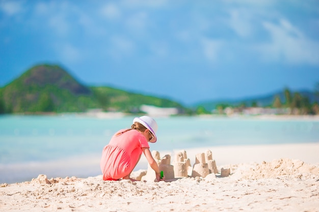 Little adorable girl at tropical beach making sand castle