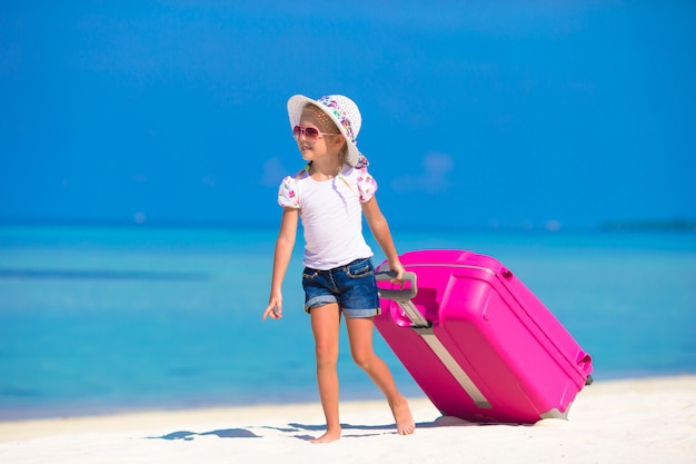 Little adorable girl with big bag on white beach 