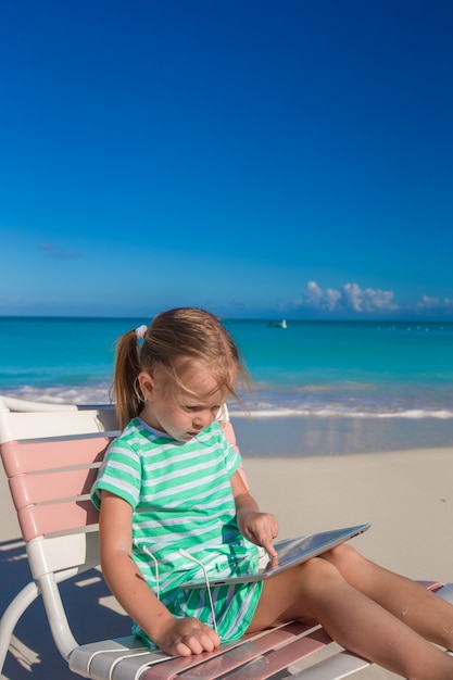 Piccola ragazza adorabile con il computer portatile sulla spiaggia durante le vacanze estive