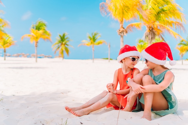 Bambine adorabili in cappelli di santa durante le vacanze di natale della spiaggia divertendosi insieme