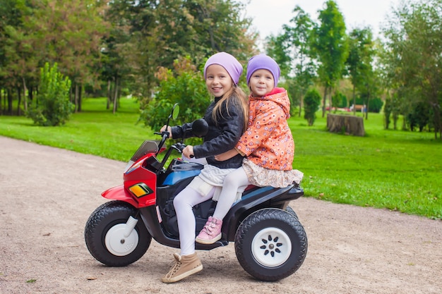 Little adorable sisters sitting on toy motorcycle in green park