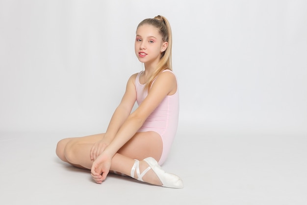 A little adorable young ballerina does ballet poses and stretching exercises on the floor at home