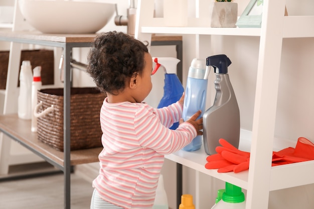 Photo little african-american baby playing with washing liquids at home. child in danger