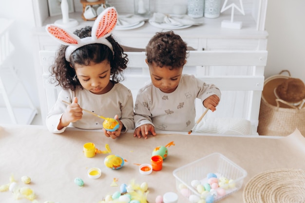 Little African American boy and girl paint Easter eggs at home black children are preparing for Easter