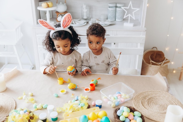 Маленькие афроамериканские мальчик и девочка красят пасхальные яйца дома черные дети готовятся к пасхе