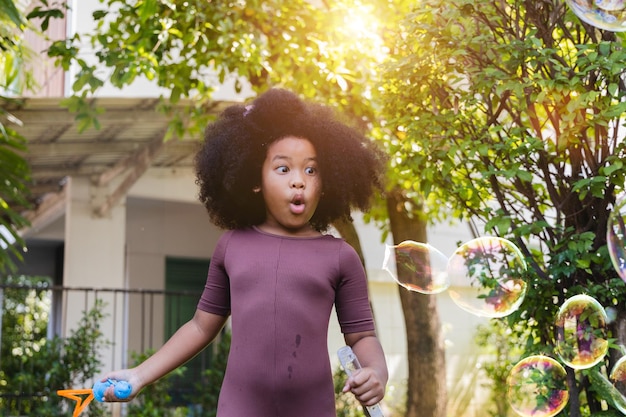 A little African American girl blowing soap bubbles in summer park