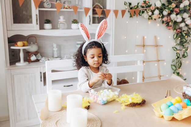 Little african american girl paints easter eggs at home in the kitchen happy easter