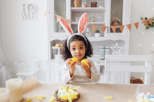 Little African American girl paints Easter eggs at home in the kitchen happy easter