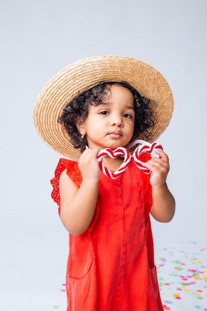 Foto piccola ragazza afroamericana in abiti estivi rossi e un cappello di paglia su uno sfondo bianco in studio