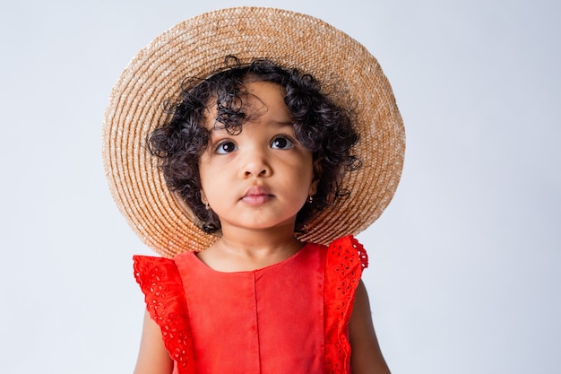 little African American girl in red summer clothes and a straw hat on a white background in the studio