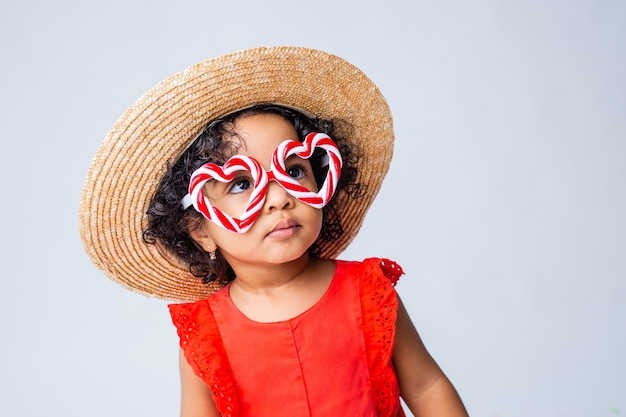 little African American girl in red summer clothes and a straw hat on a white background in the studio