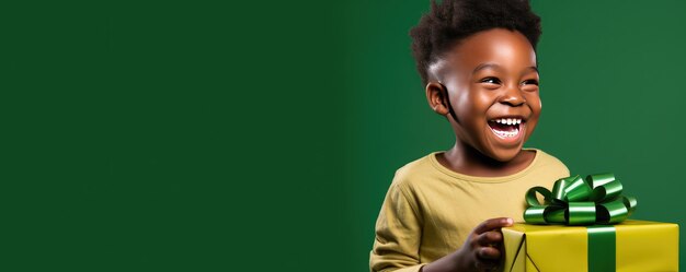 Маленький африканский мальчик раскрывает подарок и смеется на зеленом фоне.