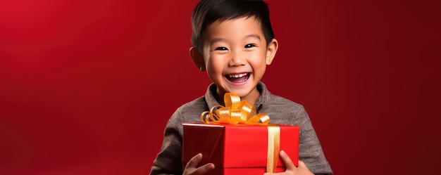 アフリカの小さな少年がプレゼントを開封し,赤い背景で笑っています. バナーコピースペース.