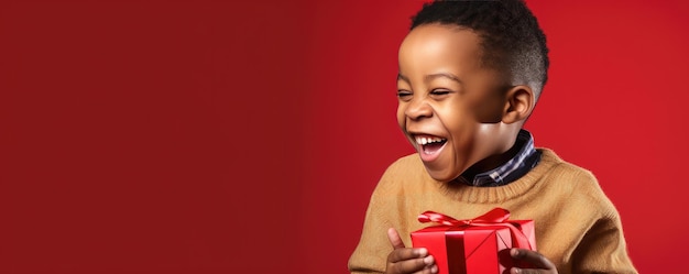 A little african boy is unwrapping a gift and laughs on red background Banner copy space Generative ai