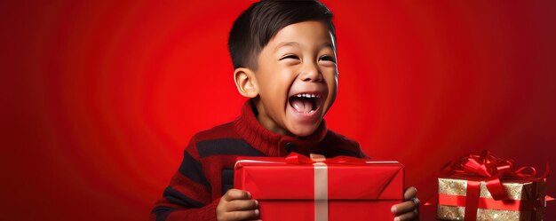 A little african boy is unwrapping a gift and laughs on red background Banner copy space Generative ai