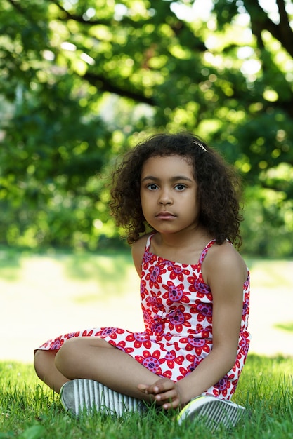 Little African girl sitting on a grass in a city park