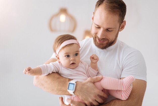 Little angel in my hands. Athletic young delighted father standing at home and holding his newborn while expressing love and care