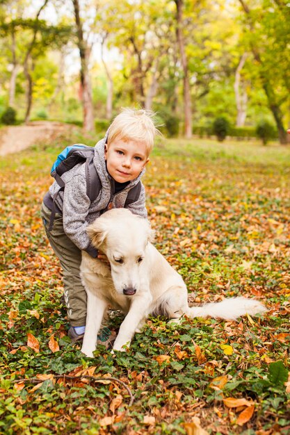 Маленький любитель животных на осенней прогулке с собакой в городском парке