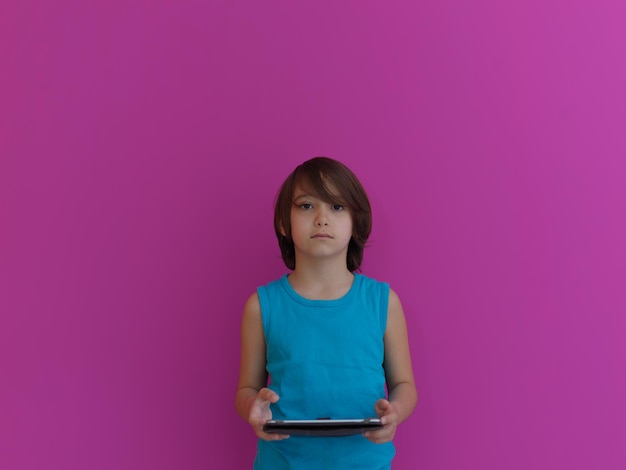 Little Arabian boy sitting using  on digital tablet. Portrait of a young arab child at home watching cartoon with pink background . Modern kid and online education elearning technology.