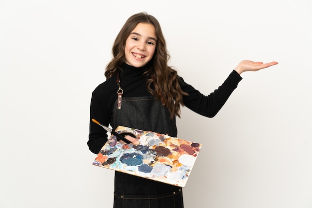 Little artist girl holding a palette isolated on white background extending hands to the side for inviting to come