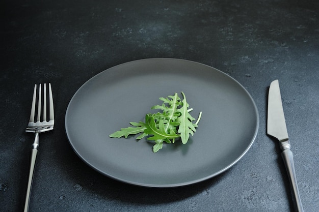 A little arugula leaves on a plate cutlery dark textured background diet weight loss veganism