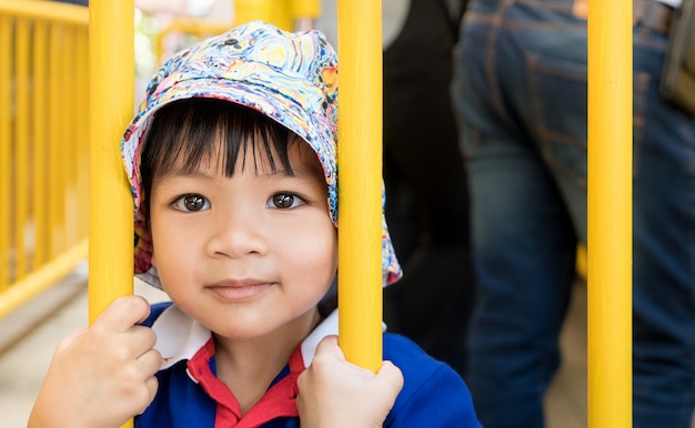 Little Asian boy hanging on a metal fence.