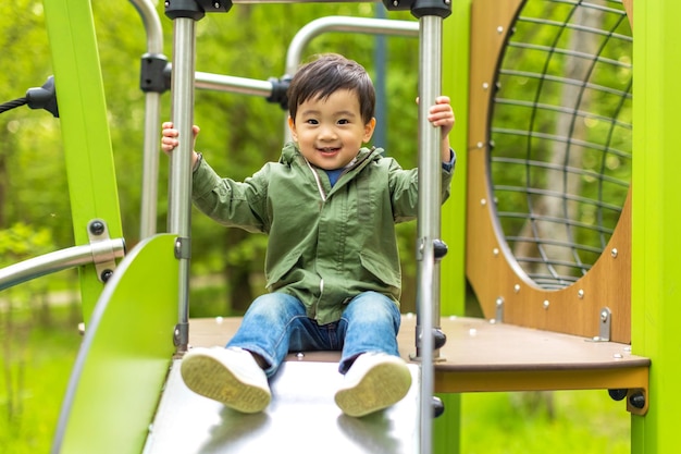 写真 小さなアジアの少年は、夏の屋外で幸せそうな顔で木製の遊び場で遊んで、笑顔でカメラを見ています