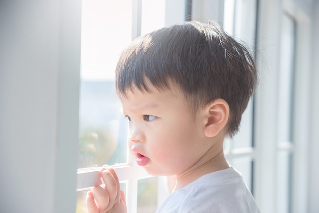 Little asian boy looking out of window in the morning