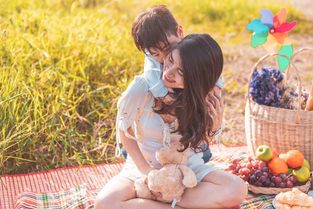 Piccolo ragazzo asiatico cavalcando sulla sua mamma super potere in prato quando si fa picnic.