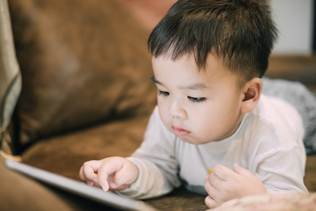 Таблетка маленького азиатского мальчика наблюдая слишком близко использующ как концепция здоровья и технологии