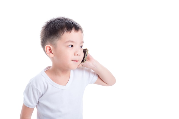 Maglietta bianca d'uso del piccolo ragazzo asiatico e parlare tramite telefono cellulare sopra fondo bianco