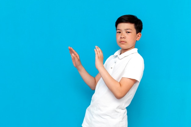 Little asian boy in white tshirt avoids and refuses on blue background korean child