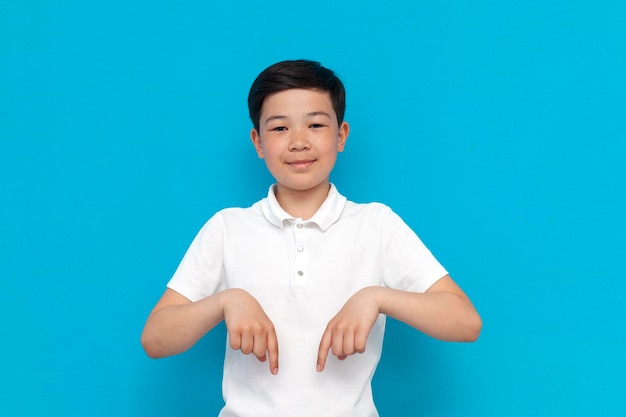 Little asian boy in white tshirt pointing down on blue background korean kid