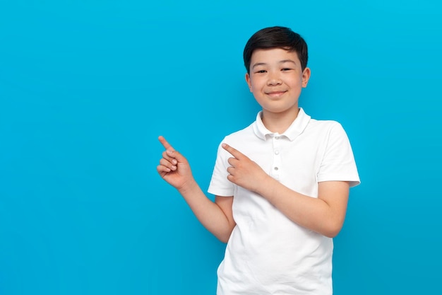 Little asian boy in white tshirt shows his hands to the side on blue background korean child