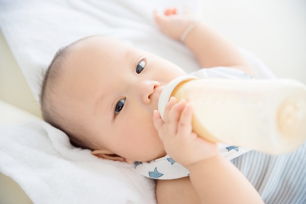 ベッドの上の哺乳瓶からミルクを飲む小さなアジアの子