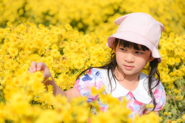 写真 アジアの幼い女の子は朝の庭で幸せに楽しみます自然にく黄色い花可愛い女の子子供明るい日に外で遊んでいる子供春の美しい花