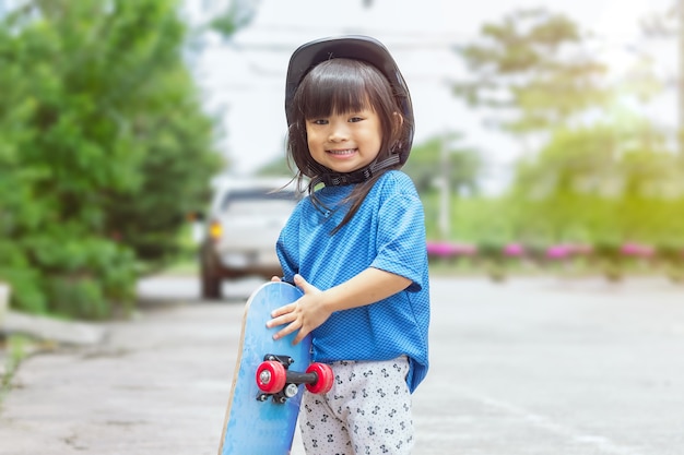 小さなアジアの子供の女の子が遊んでスケートボードに乗っている彼女は公園で安全ヘルメットをかぶっています