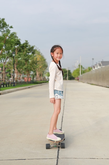 Little Asian child playing on skateboard. Kid riding on skateboard outdoors at the street