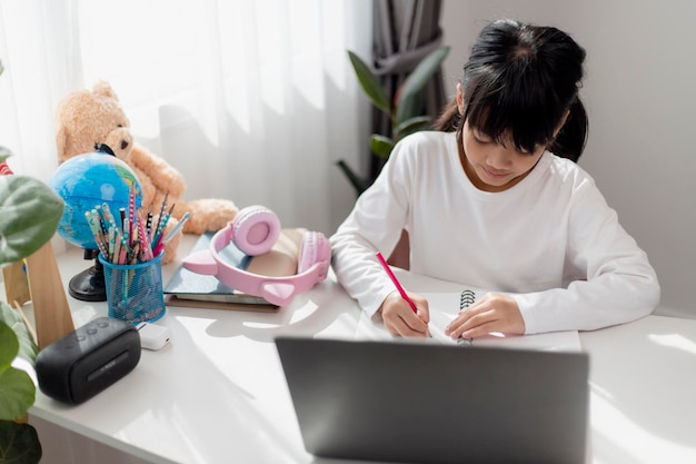 Little Asian girl doing her homework with laptop