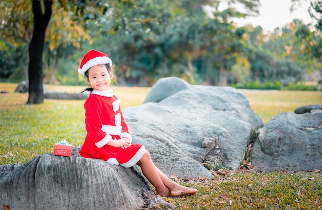 写真 公園のプレゼントボックスと赤いサンタクロースの衣装を着た小さなアジアの女の子