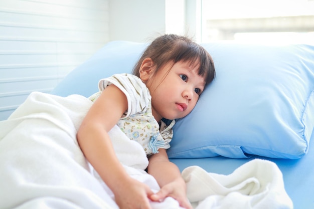 A little Asian girl is sick with a fever She was lying on the bed in the hospital examination room concept of children's disease viral infection medical services