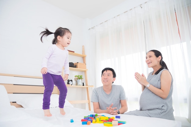 Little asian girl jumpping on bed while her mother sing a song and clapping hands