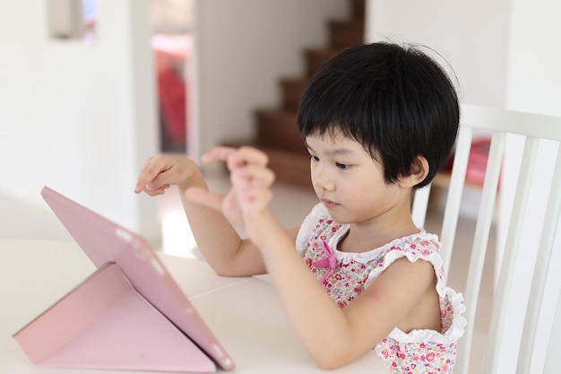 Little asian girl playing digital tablet at home