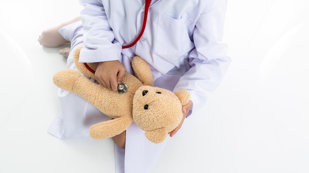 Foto piccola ragazza asiatica che gioca a fare il dottore e ascolta l'orso di peluche con lo stetoscopio ragazza asiatica