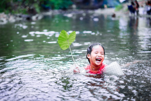 Piccola ragazza asiatica che gioca acqua con foglia di loto nel flusso naturale