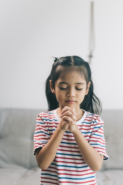 家で手を握り合って祈るアジア人の少女