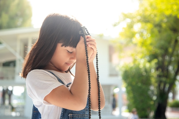 Little Asian girl praying with holding the cross, Christian concept.