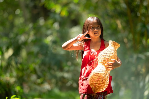 Little asian girl in red dress holding fishing equipment in the forest