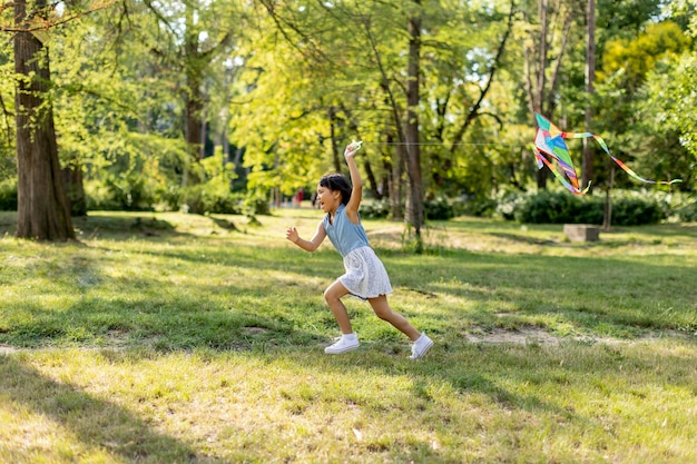 Bambina asiatica che corre felicemente con un aquilone nel parco