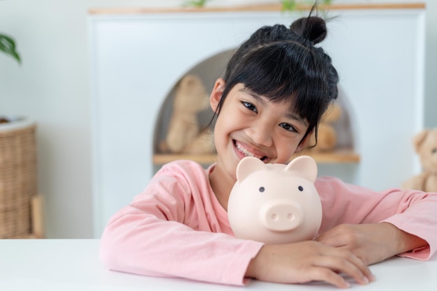 Little Asian girl saving money in a piggy bank, learning about saving, Kid save money for future education. Money, finances, insurance, and people concept